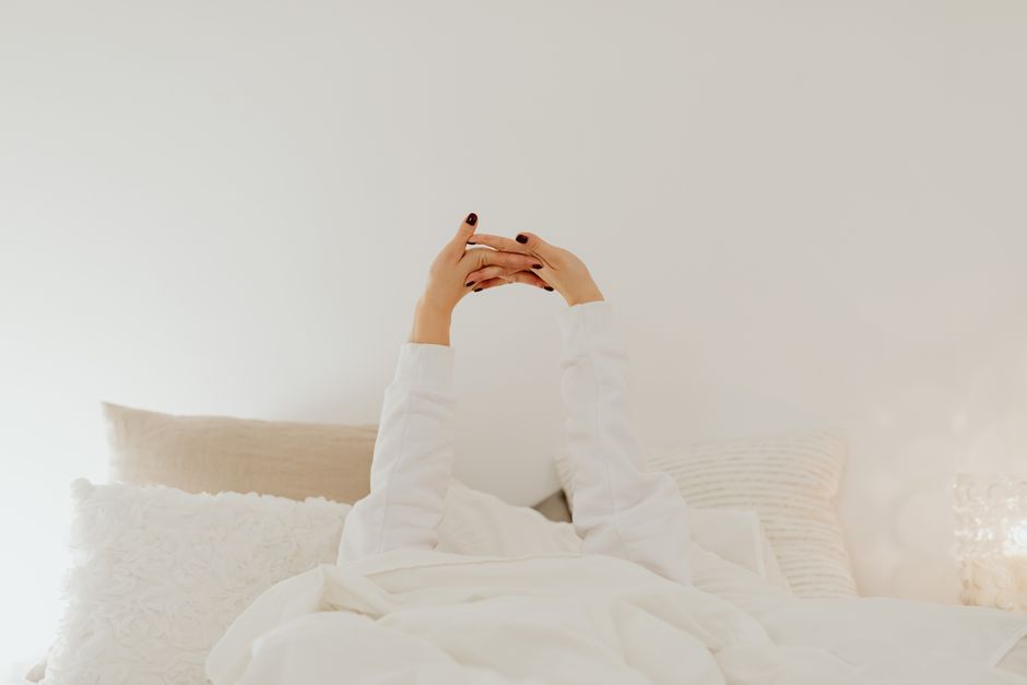 Person waking up in bed with hands clasped and fingers stretched, illustrating morning finger stiffness