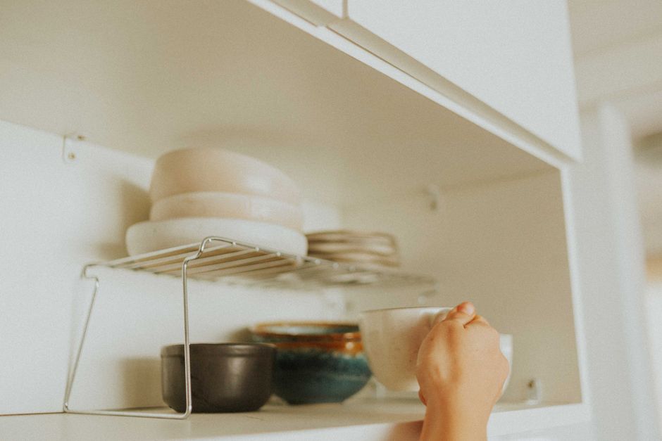 Adult reaching overhead toward a high shelf, a motion that commonly triggers shoulder impingement pain.